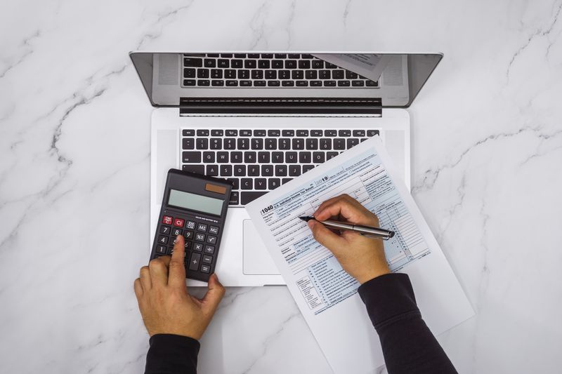 Person using a calculator and holding a pen over tax papers