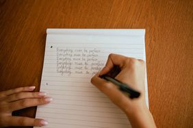 A person writing repetitive sentences in a notebook on a wooden surface