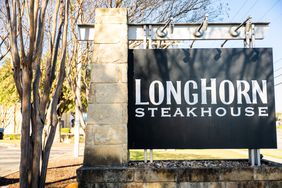The LongHorn Steakhouse logo is seen on a sign next to trees and a parking lot.