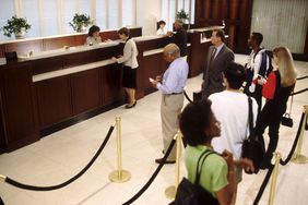 Several customers queue in the lobby of a large bank while tellers assist other customers at counters.