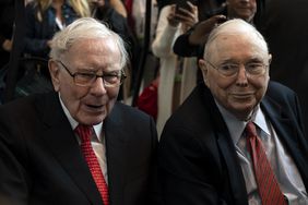 Warren Buffett and Charlie Munger seated together at an event, surrounded by people
