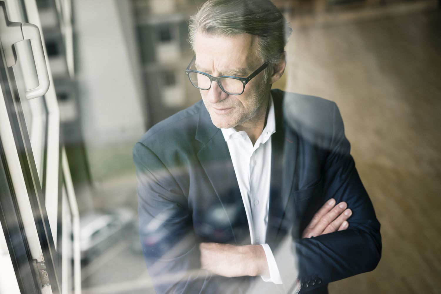 A businessman looking out the window with his arms crossed.