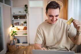 A happy man looks at a computer, holding up a bank card.