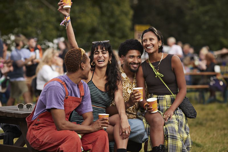 A group of four young adults sitting together, smiling and holding cups outdoors