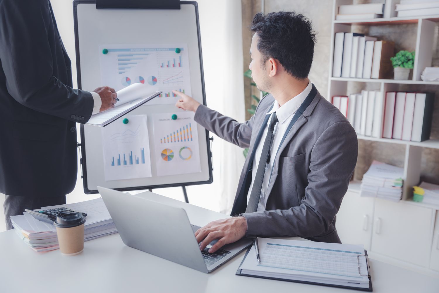 An accountant points to a display board holding charts and explains quarterly company earnings after tax during a meeting.