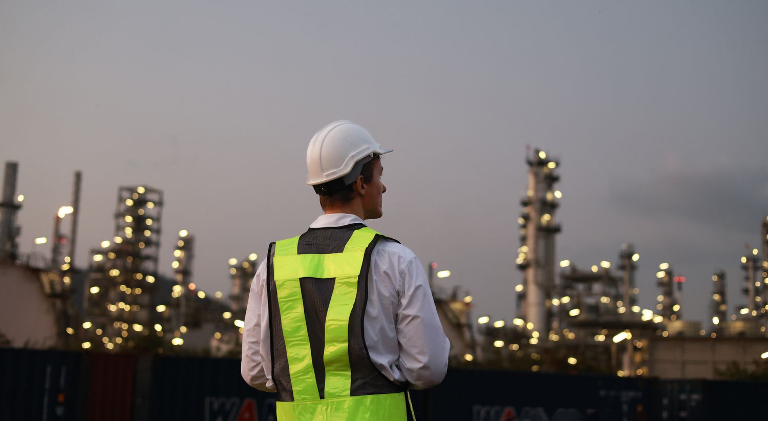 A chemical engineer working the night shift at a petroleum oil refinery stands on a rooftop to observe the lights of the refinery.