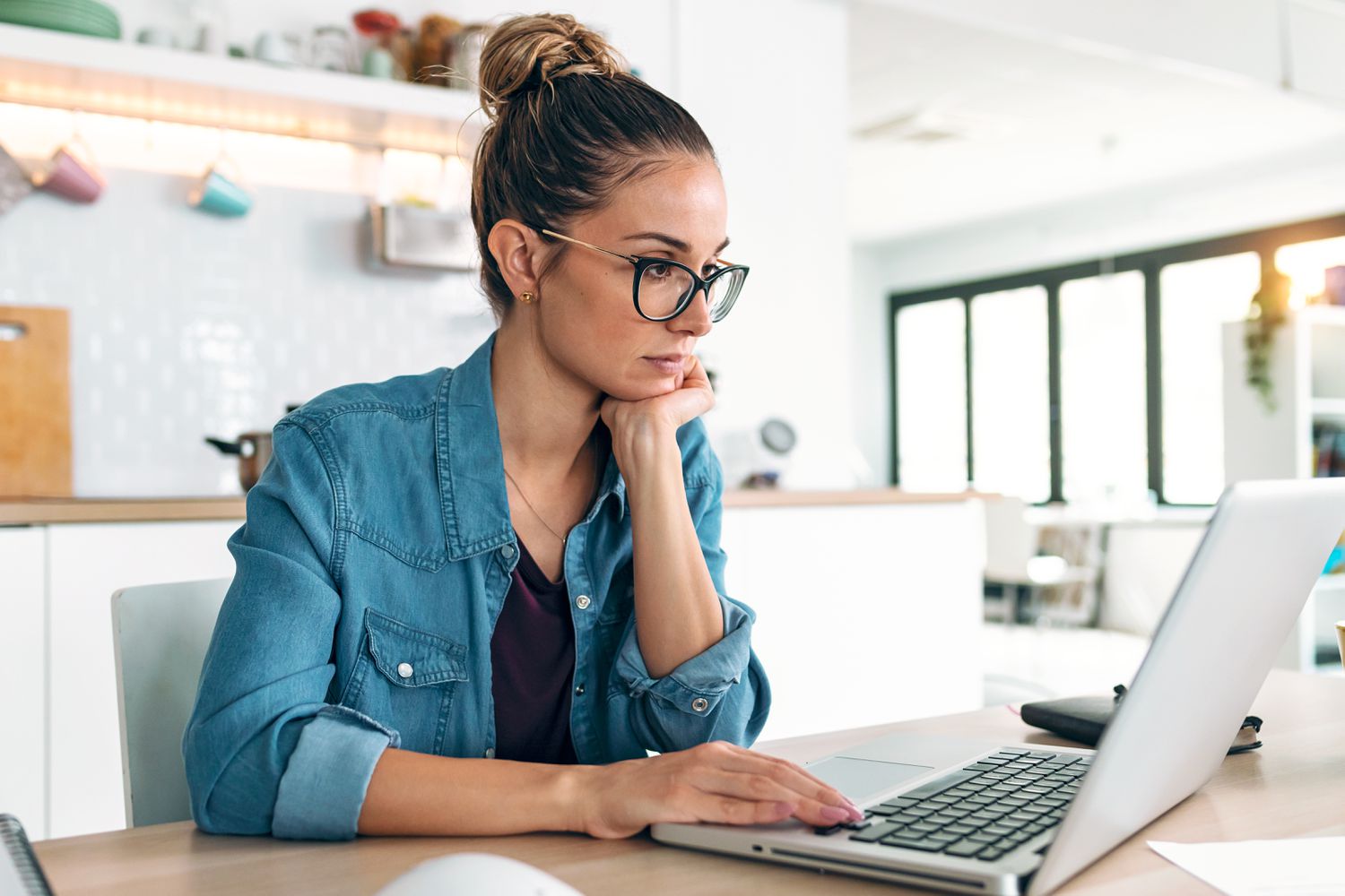 Young woman sitting in her kitchen and looking at bank rates on her laptop
