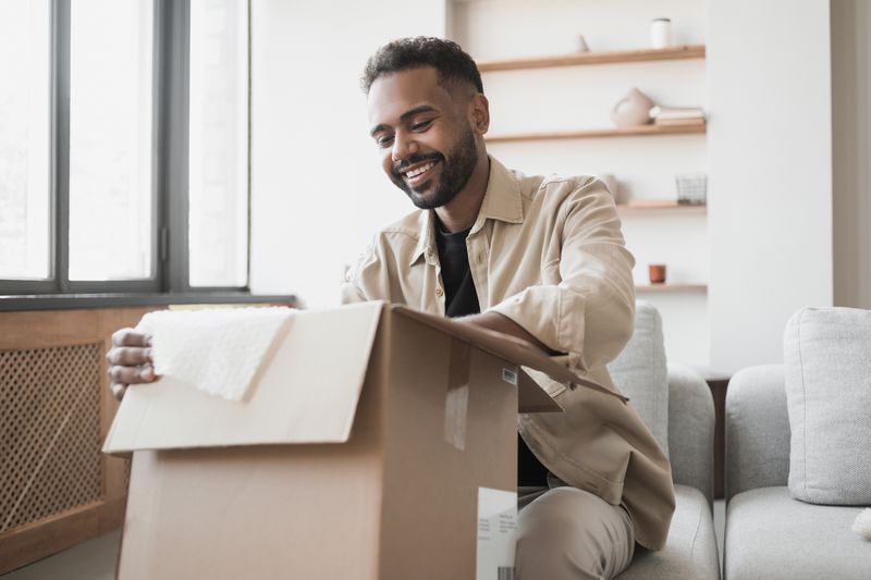 Happy man opens big box while sitting on couch.