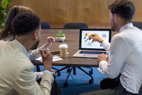 People in an office discussing data on a laptop.