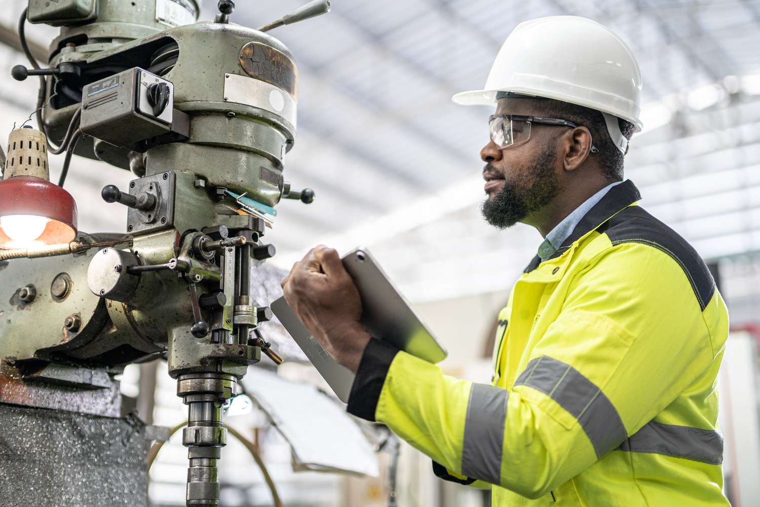 An engineering worker inspects a drillpress machine for usefulness at a manufacturing plant.