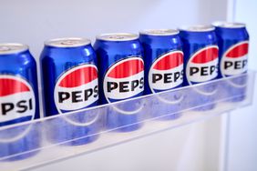 A row of blue Pepsi cans sit in a refrigerator shelf.