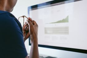 A close up of a person, holding their glasses and looking at their computer screen. 