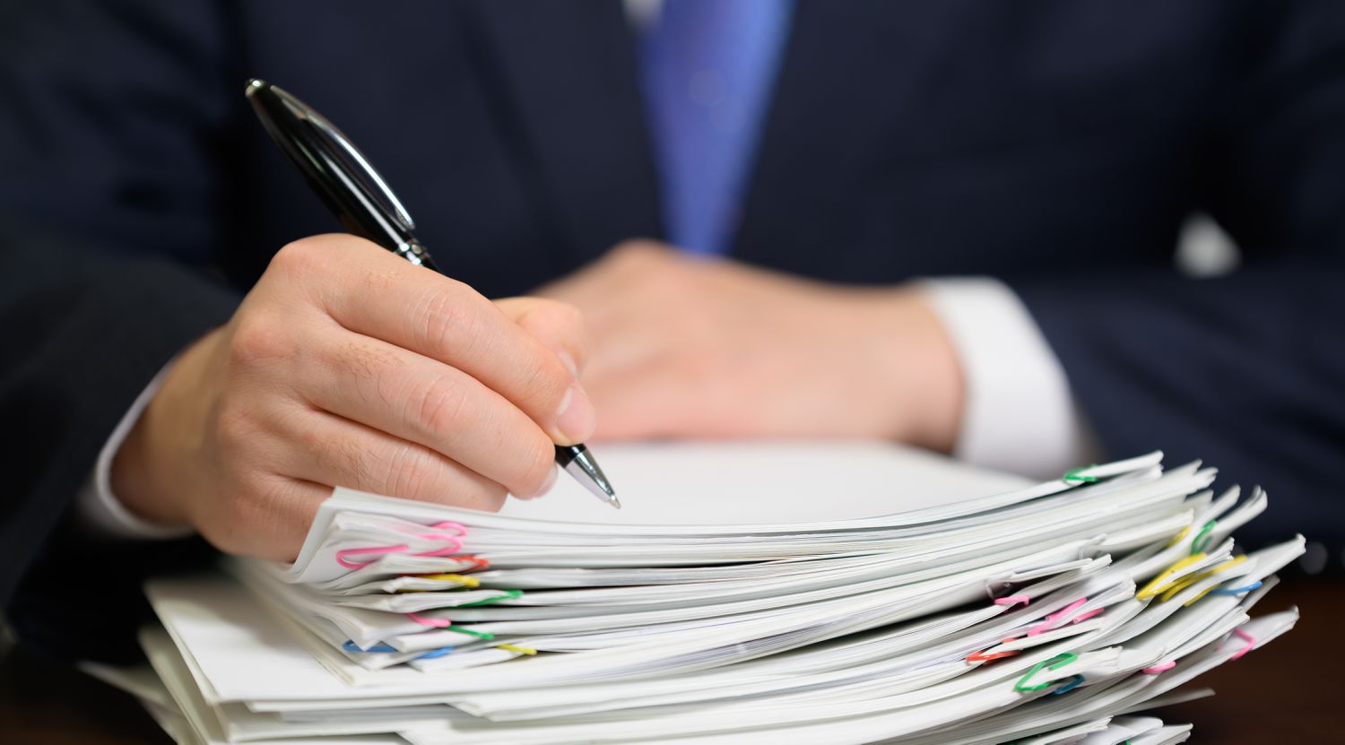 Business person holding a pen and signing a stack of paperwork 
