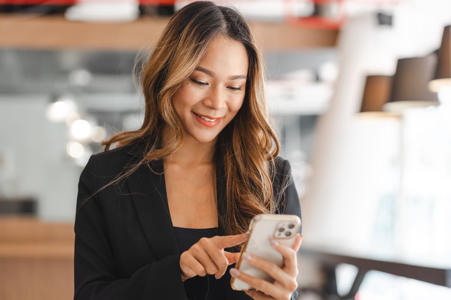 Young professional Asian woman smiles while looking at smartphone
