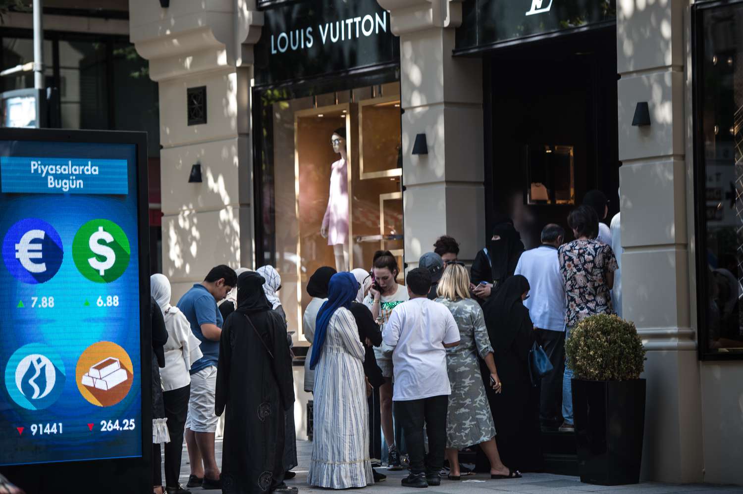 A group of people standing beside a signage of currency symbols.