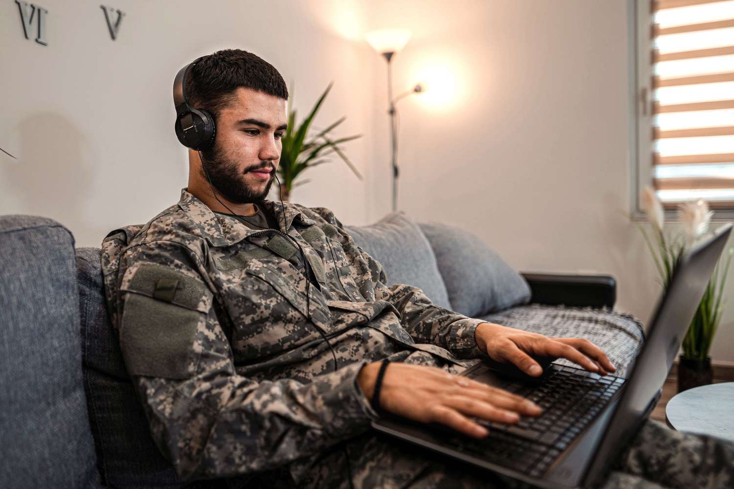 Soldier working on a laptop with headphones on while seated on a couch