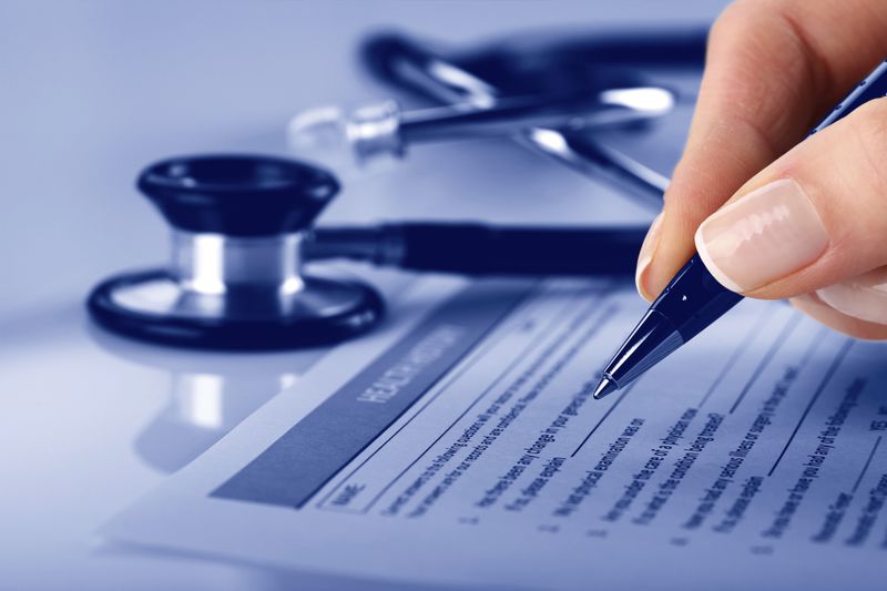 Person's fingers signing medical insurance form