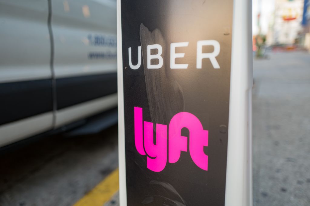 Close-up of vertical sign with logos for ridesharing companies Uber and Lyft, with wheels of a car in the background, indicating a location where rideshare pickups are available in downtown Los Angeles, California, October 24, 2018. 