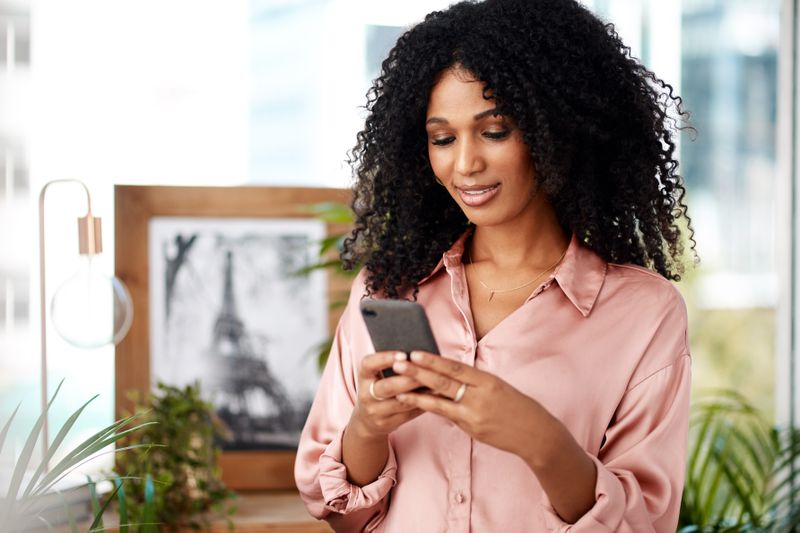 Young woman at home, looking at banking info on her phone and smiling