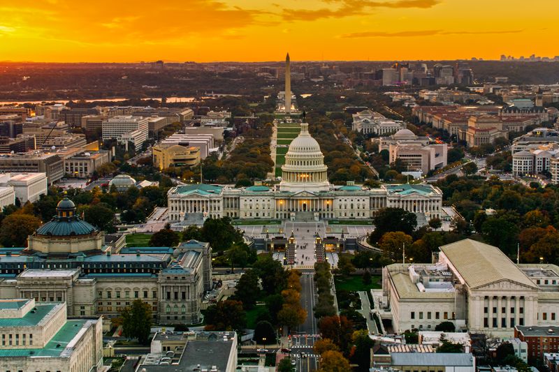Helicopter shot of the United States Capitol and Supreme Court Building in Washington, D.C. at sunset, with the National Mall in the background.