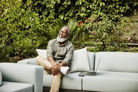 Medium wide shot portrait of smiling senior man with laptop sitting in garden on rooftop deck