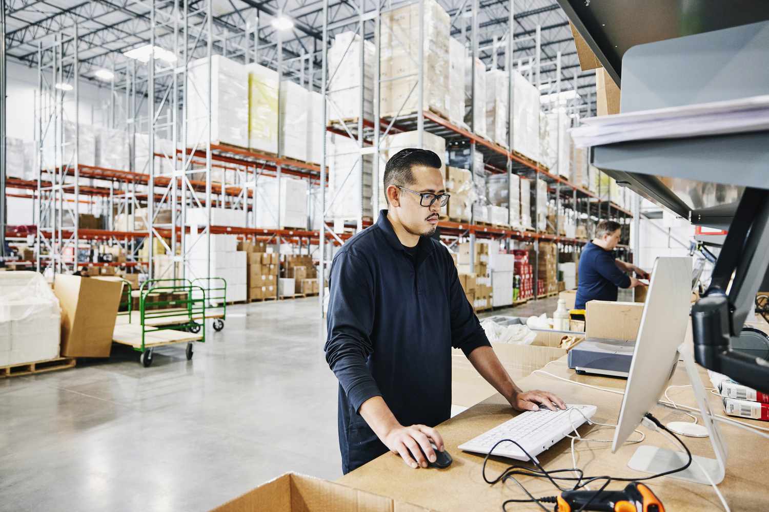 Warehouse worker using a computer inside with a wide shot of the warehouse interior