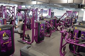 Purple, black, and yellow gym equipment is seen inside a Planet Fitness gym.