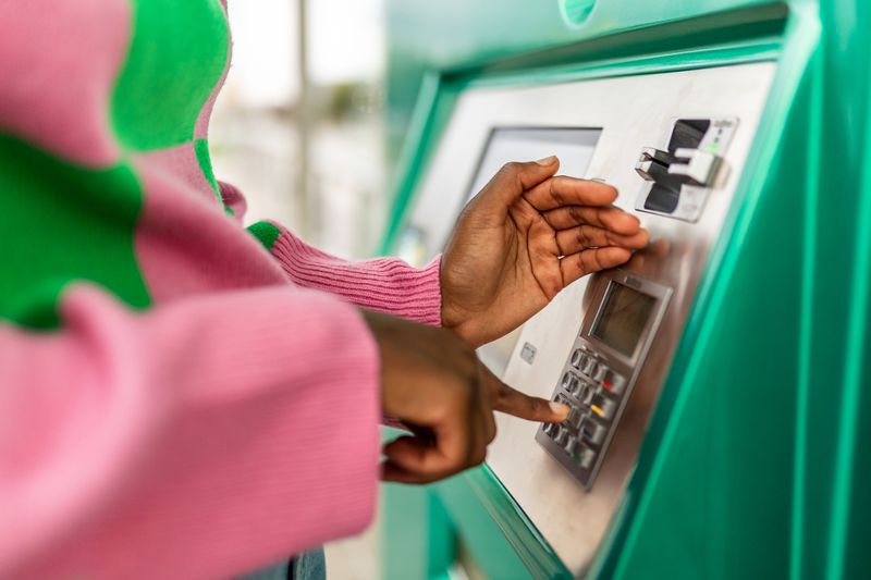 Person inputting pin number on ATM machine, hovering over with one hand to hide it from others.