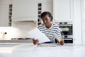 A woman stands at a kitchen island looking at paperwork