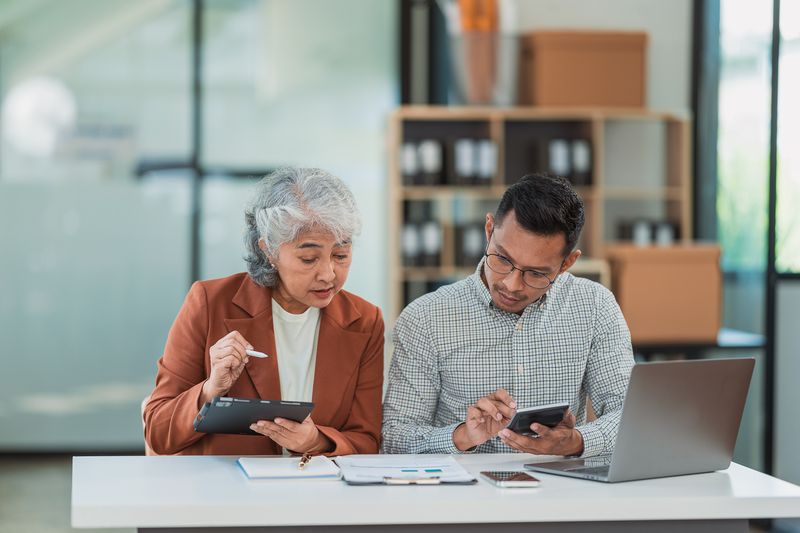 Senior business woman and young man working together analyzing finances