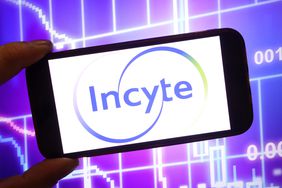 The purple and green Incyte logo is seen on a phone screen in front of a purple and white stock chart background.