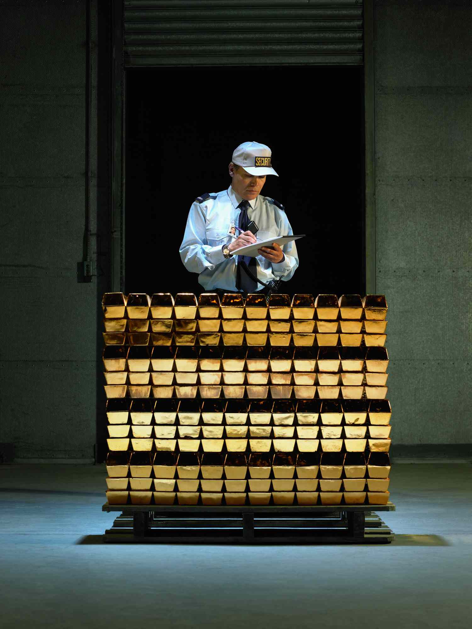 Security guard with clipboard and pen by stack of gold bars.