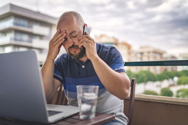 A Man Clutches His Head as He Talks on the Phone