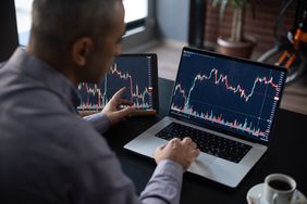 Person uses two laptops to compare charts showing stock price and volume of two different investments.
