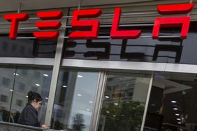A person walks in front of a Tesla dealership in Lisbon, Portugal with a red TESLA sign overhead.