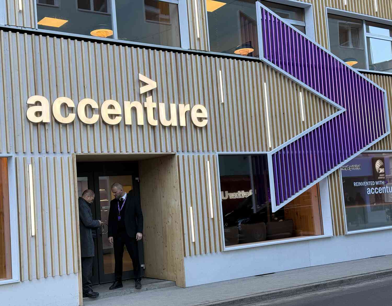 The Accenture logo is seen above the entrance to an office building, with a large purple logo to the right.