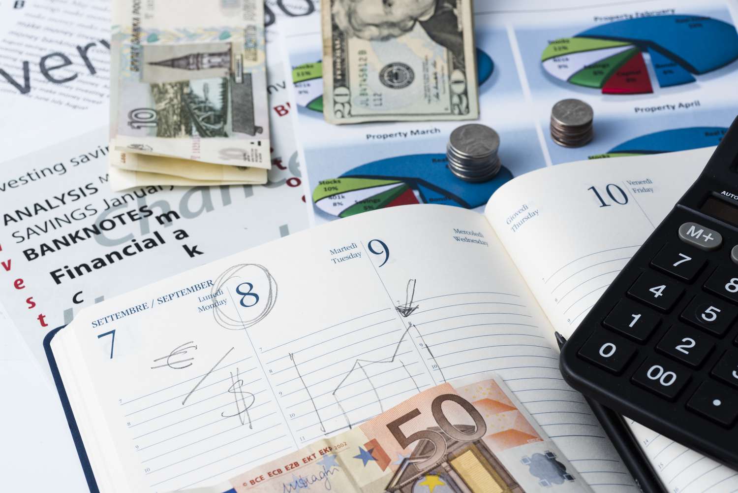 An appointment book shows a marked date with a note to exchange euros for U.S. dollars and laying around the book are stacks of various currencies.