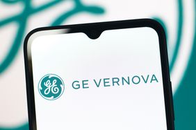 The green GE Vernova logo is seen on a phone screen, with a larger version in the background.