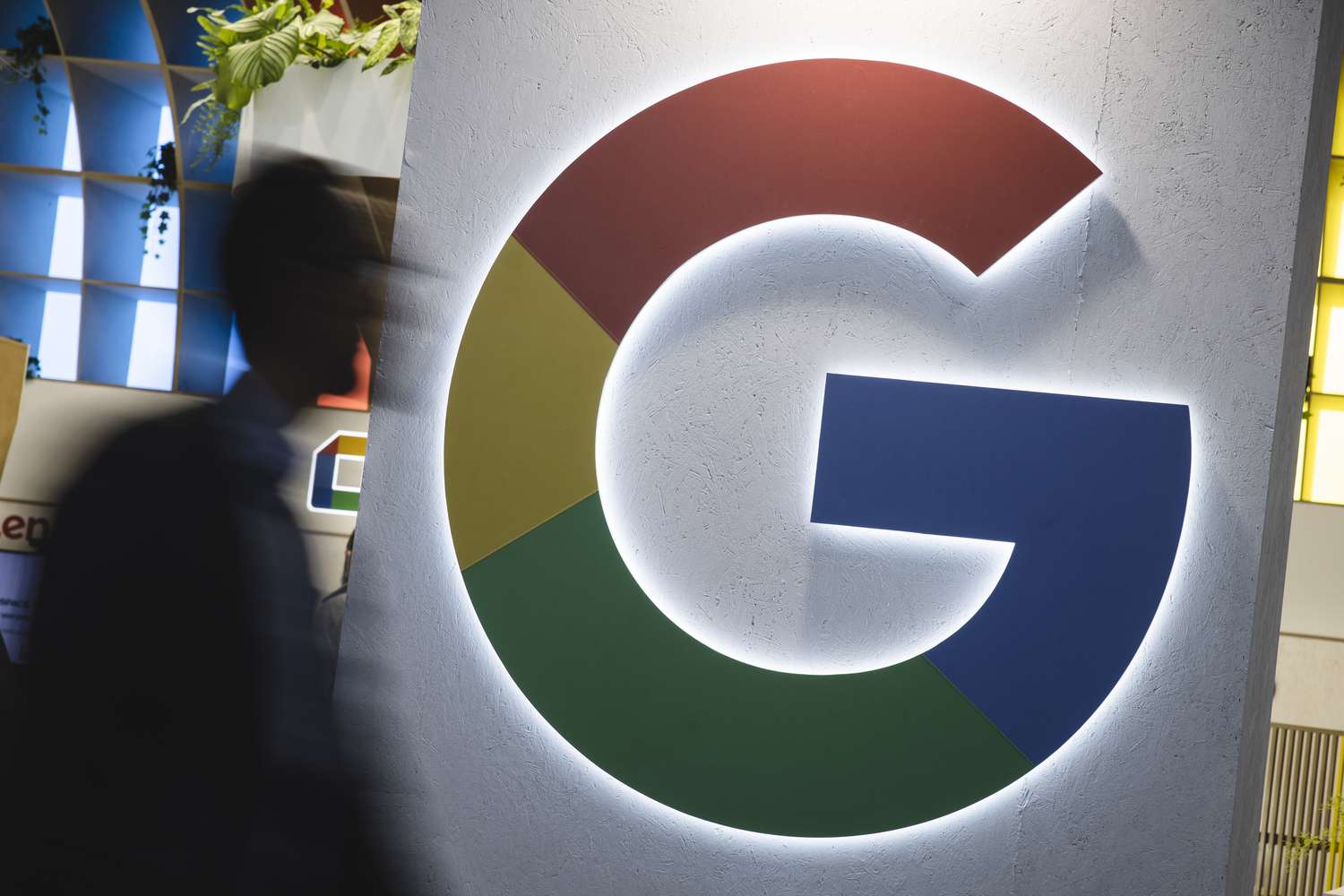 The multi-colored Google 'G' on a wall with a person walking by.