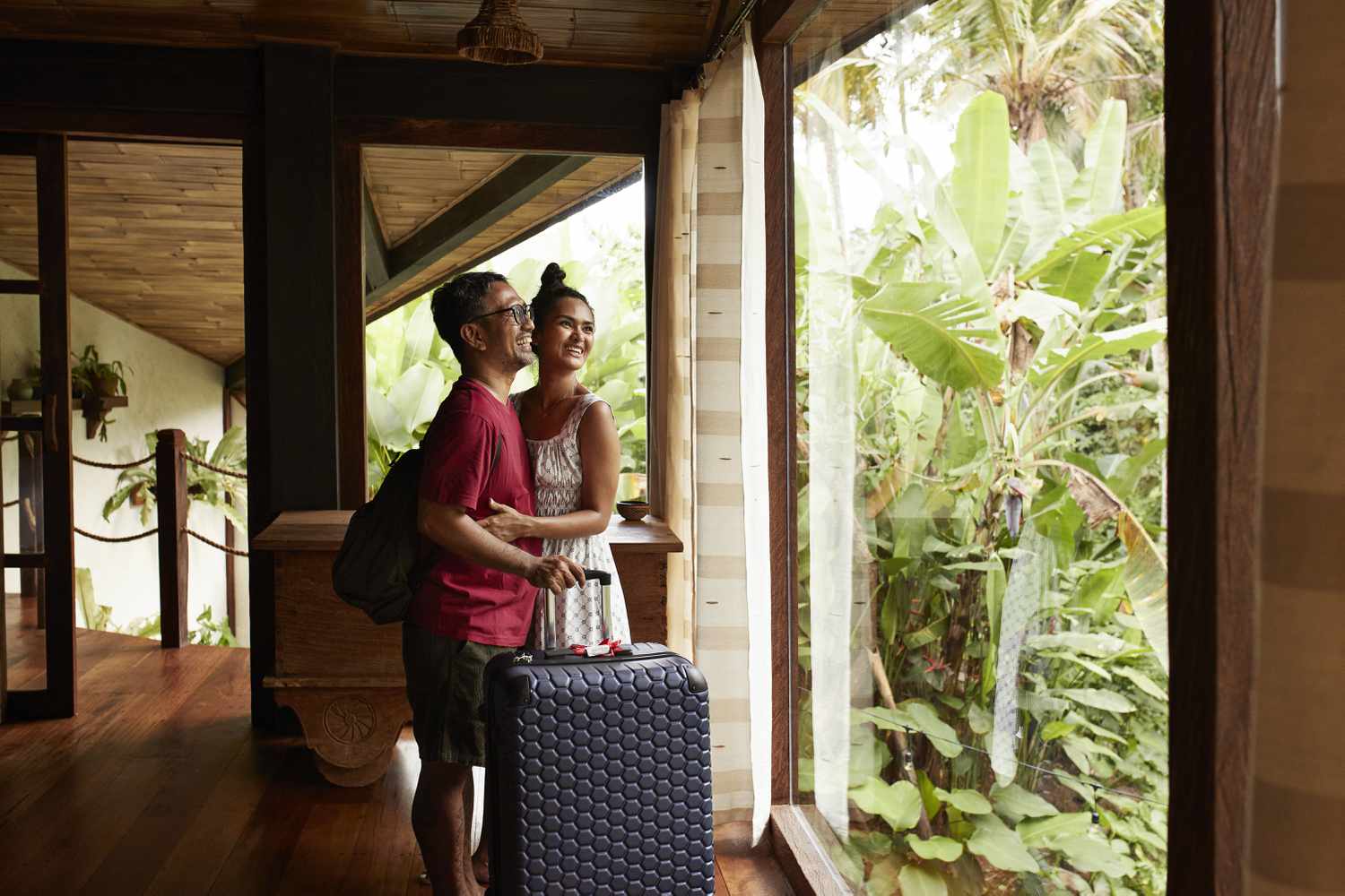 Happy man and woman with luggage standing near window during vacation