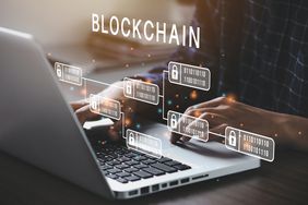 A person typing at a laptop with illustrations of the blockchain floating over the keyboard.