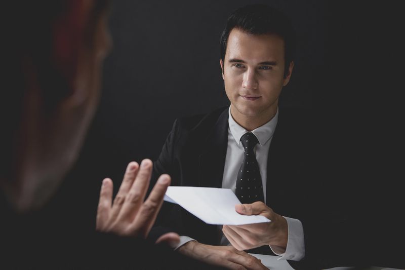 A businessman rejecting bribe money in white envelope offered by his partner.