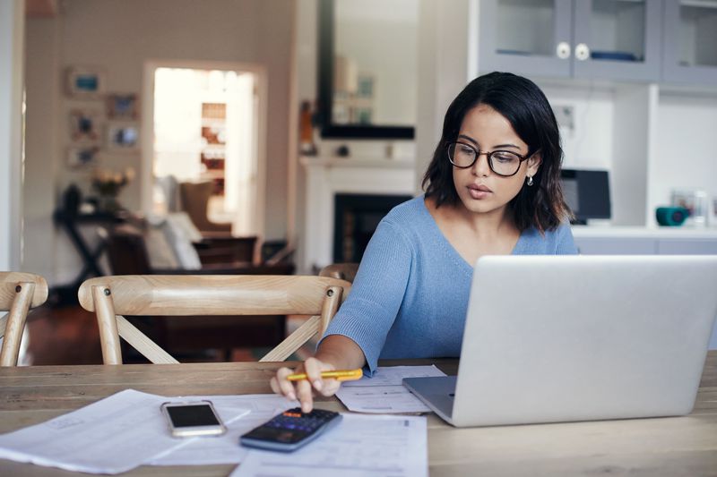 Shot of a young woman using a laptop and calculator while working from home.