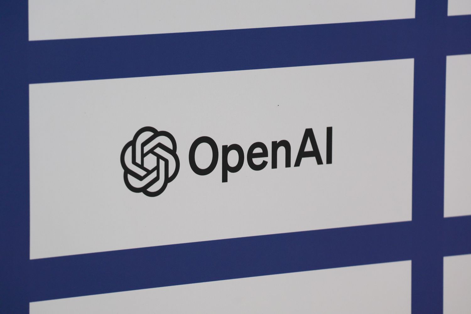 The black OpenAI logo is seen on a white and blue background.