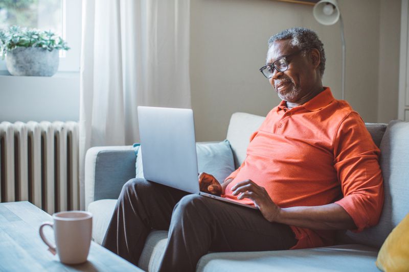Mature man at home, sitting on sofa and using laptop.