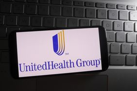 The blue and yellow UnitedHealth Group logo is seen on a phone screen, sitting on a laptop keyboard.