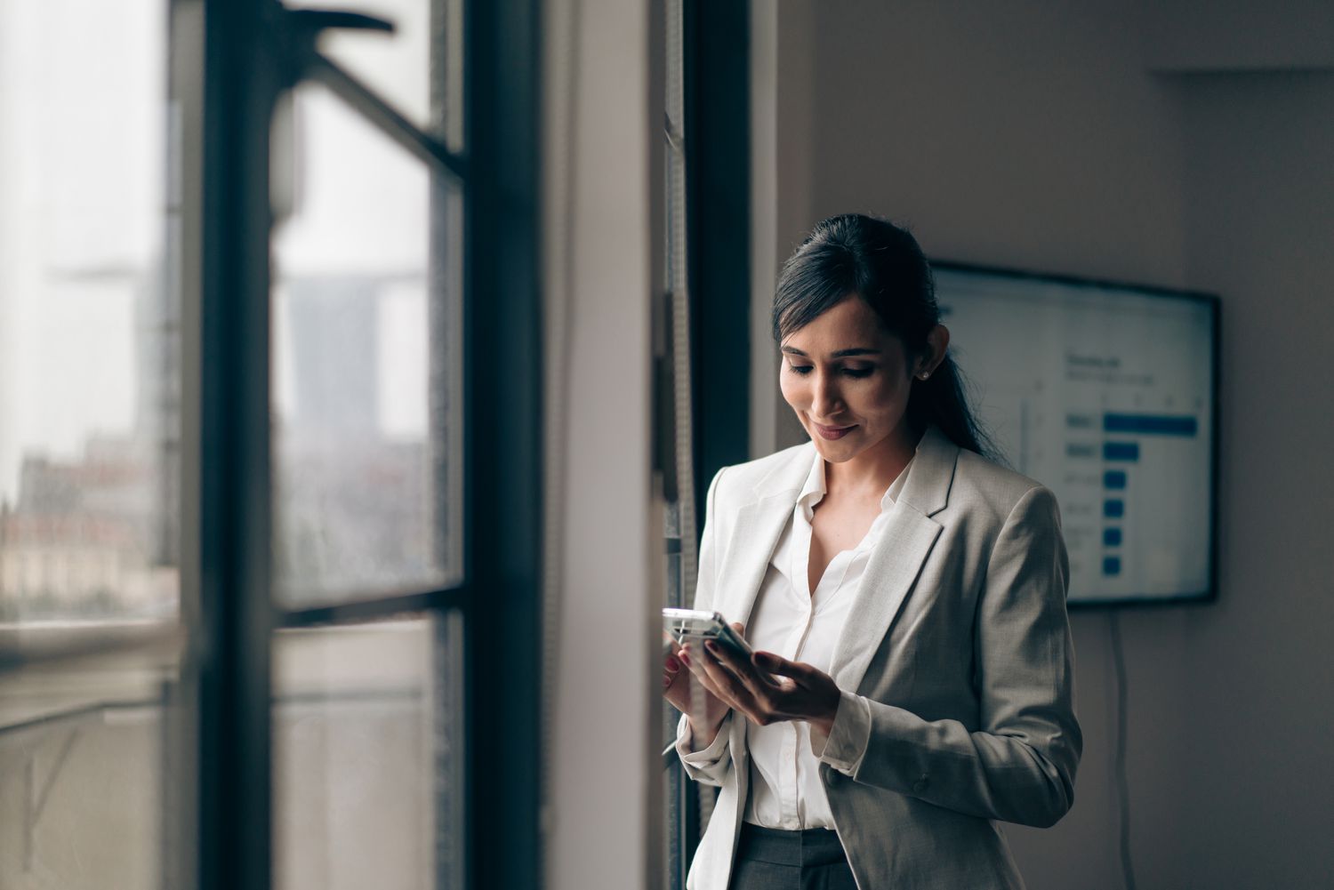 Woman in business attire looking down at a mobile phone.