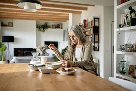 A woman sits at a table eating breakfast and reading a document