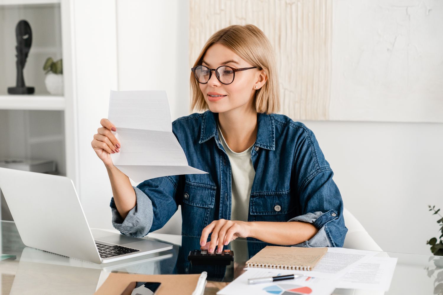 Young woman looking at paperwork in front of her laptop.
