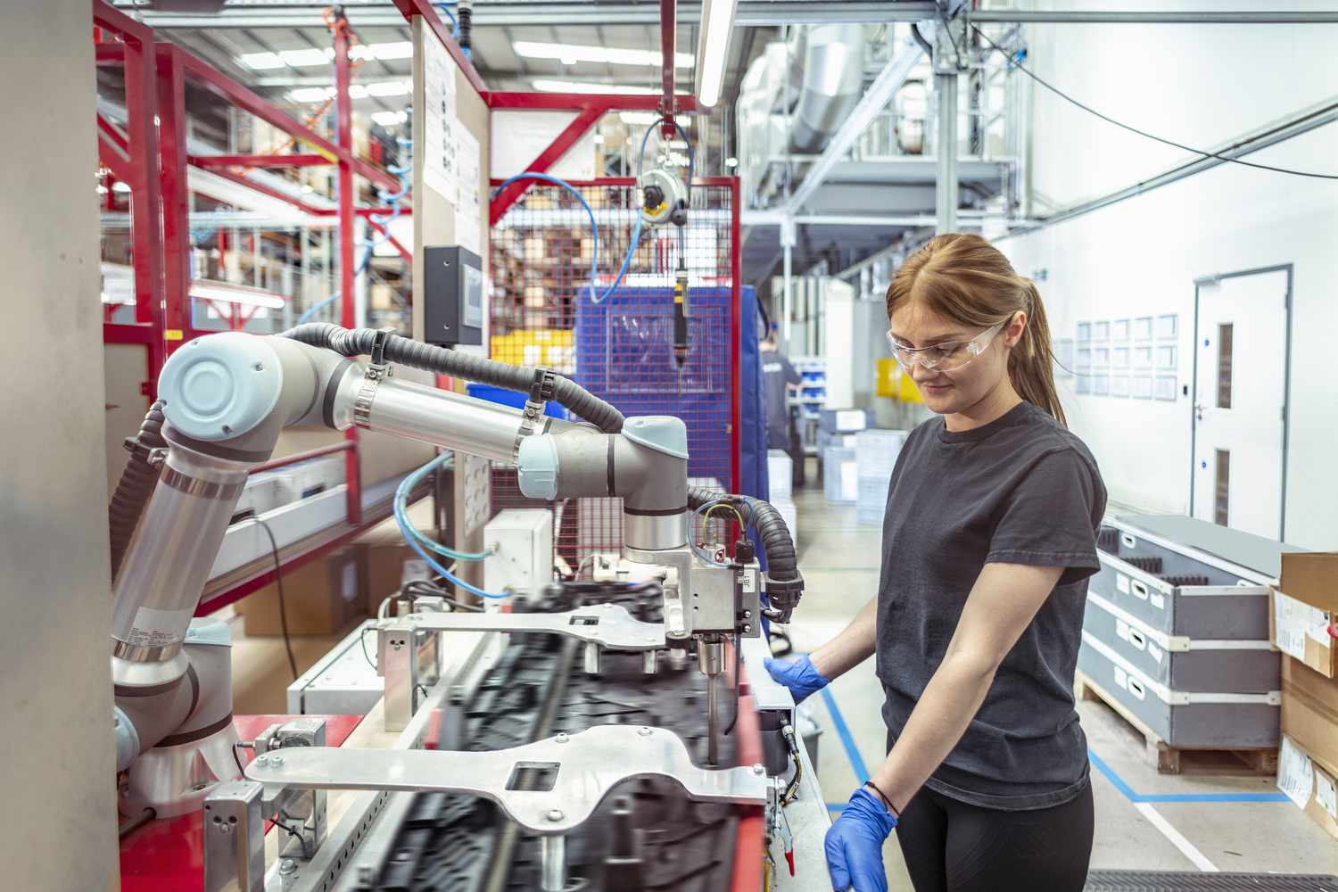 Female worker working with cobot, a collaborative robot, in robotic assembly machine in automotive parts factory